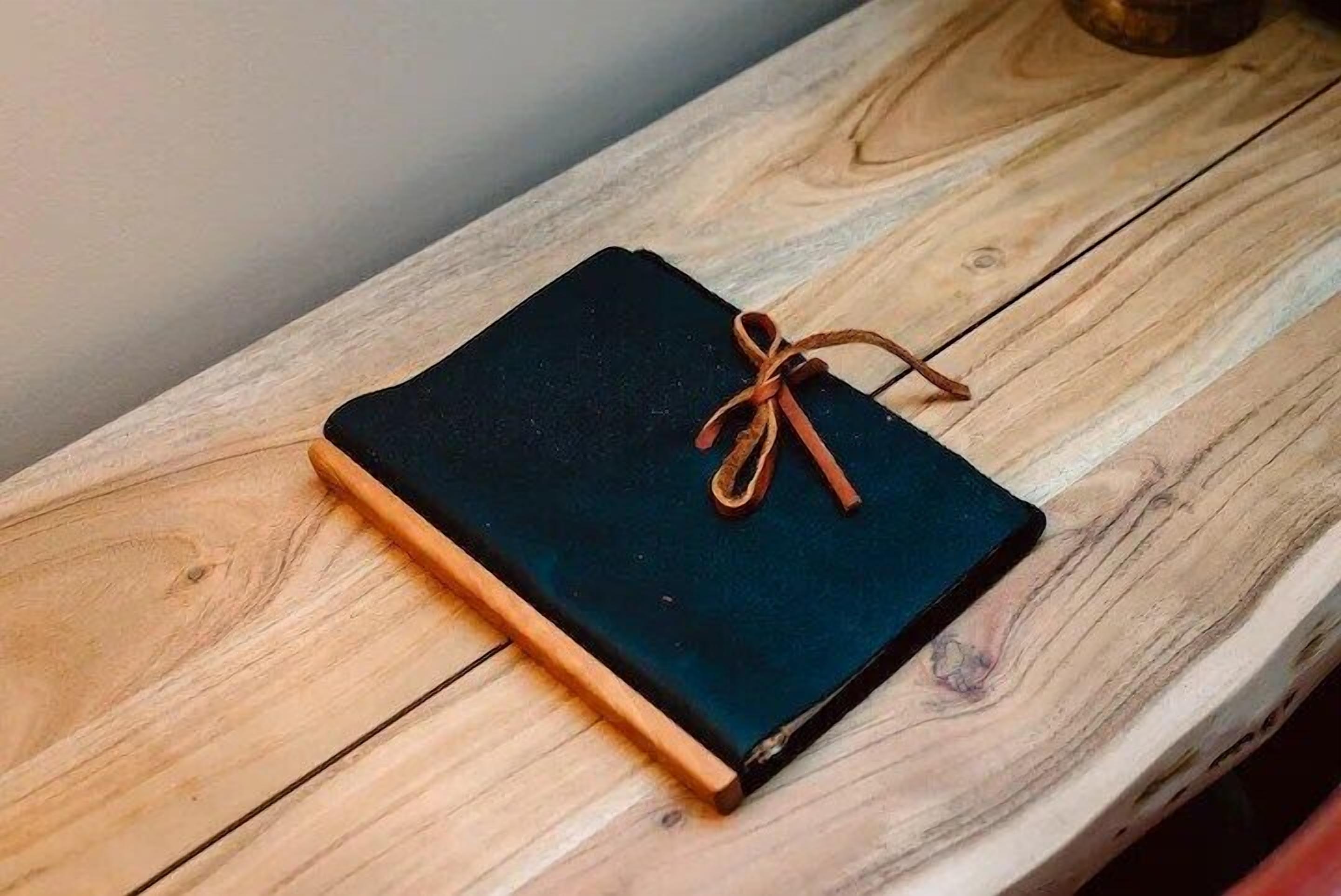 A black notebook with a brown ribbon bookmark on a wooden table.