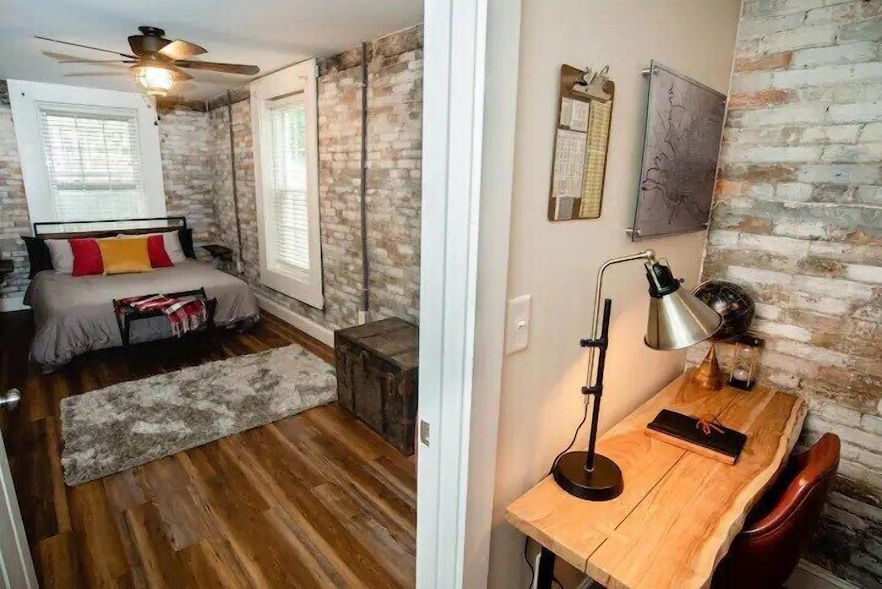 A bedroom with a bed, a desk, a chair, a lamp, and a brick wall.