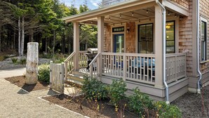 A two-story house with a porch, a front door, and a small outdoor seating area. - Seabrook Cypress and Sand | Hot Tub, Park Views | 3BR, Sleeps 8, Cedar Run Park (Pacific Beach)