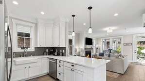 A modern kitchen with white cabinetry, a central island, pendant lighting, and a view into the living area. - Seabrook Cypress and Sand | Hot Tub, Park Views | 3BR, Sleeps 8, Cedar Run Park (Pacific Beach)