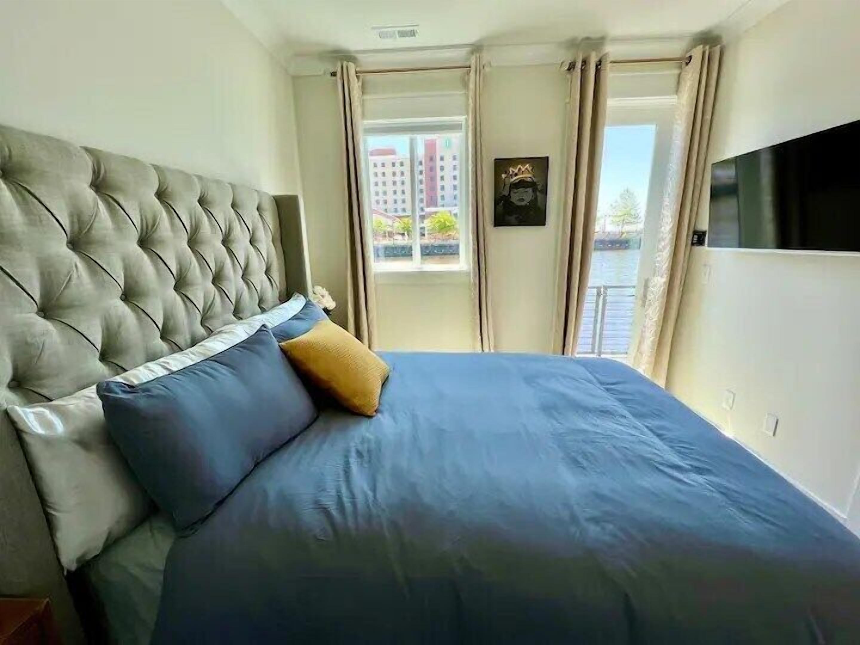 A hotel room with a large bed, a television, and a view of a cityscape through the window.