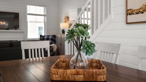 Ein Essbereich mit Holztisch, einem gewebten Korb und einer Glasvase mit Grünpflanzen.