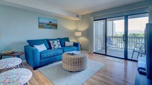 Ein Wohnzimmer mit einem blauen Sofa, einem runden Hocker, einem kleinen Tisch und einem Gemälde an der Wand.