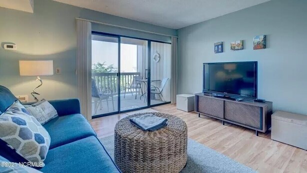 Ein Wohnzimmer mit einem blauen Sofa, einem Fernseher und einem Balkon mit einer Schiebetür.