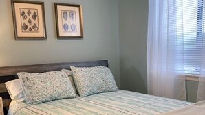 Ein Schlafzimmer mit einem Bett, zwei gerahmten Bildern an der Wand und einem Fenster mit Vorhängen.