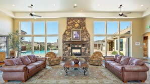 A spacious living area with a stone fireplace, leather sofas, and large windows offering a view of a pool. - Gateway to Fun: Private Hot Tub, Community Pools, Bbq (Washington)