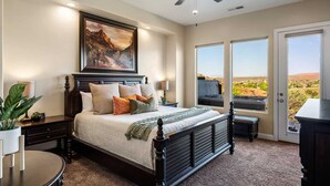 A bedroom with a large bed, a ceiling fan, a painting, and a view of the desert through the window. - Gateway to Fun: Private Hot Tub, Community Pools, Bbq (Washington)