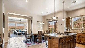 A spacious kitchen with a large island, a dining area with chairs, and a view of a desert landscape through large windows. - Gateway to Fun: Private Hot Tub, Community Pools, Bbq (Washington)