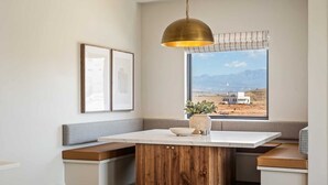 A modern kitchen with a central island, wooden cabinetry, a large window with a view of a desert landscape, and a hanging pendant light. - A Bit of Paradise: Desert Color Lagoon + Beaches (St George)