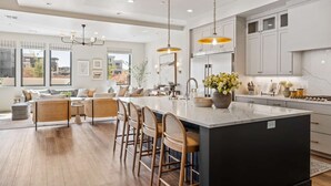 A modern kitchen with a large island, bar stools, pendant lighting, and a view of the outside through large windows. - A Bit of Paradise: Desert Color Lagoon + Beaches (St George)