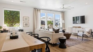 Un salon moderne avec une table à manger en bois, un canapé blanc et un téléviseur à écran plat fixé au mur.