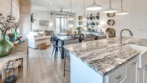 A modern kitchen with a marble countertop, pendant lights, and a dining area with a glass table and chairs. - Residence Club Unit 6 in Carlton Landing (Carlton Landing)