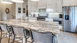 A modern kitchen with white cabinets, a large granite island, stainless steel appliances, and pendant lighting. - Residence Club Unit 6 in Carlton Landing (Carlton Landing)