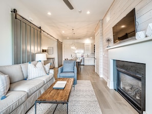 A modern living room with a sofa, armchair, coffee table, fireplace, and kitchen in the background.