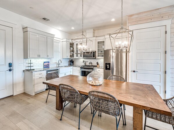 A modern kitchen with white cabinets, a stainless steel refrigerator, and a wooden dining table with wicker chairs.