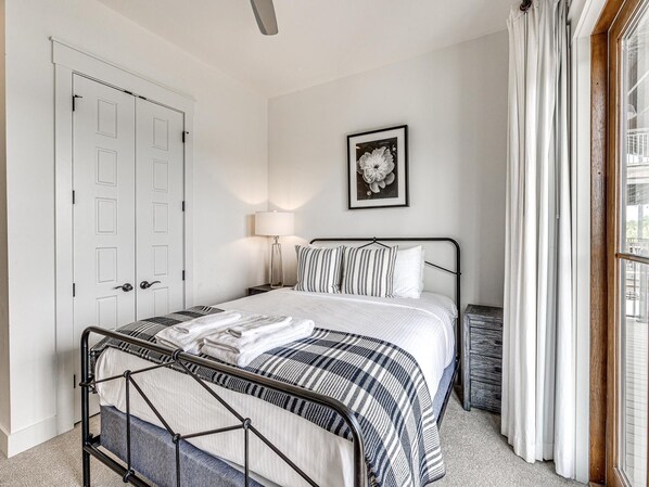 Un dormitorio con cama, mesita de noche, lámpara, un cuadro enmarcado en la pared y una ventana con cortinas.