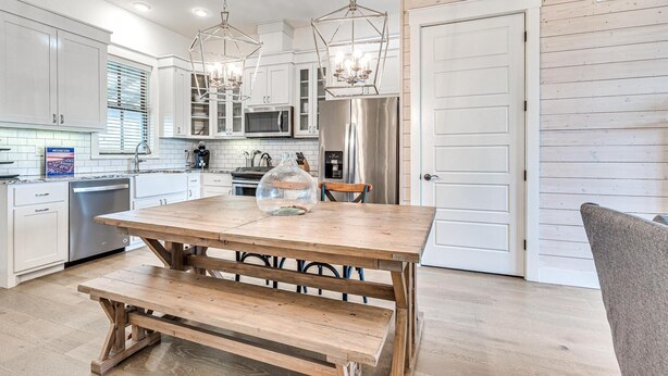 Una cocina moderna con armarios blancos, electrodomésticos de acero inoxidable y una mesa de comedor de madera con bancos.