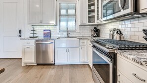 Una cocina moderna con armarios blancos, lavavajillas de acero inoxidable, horno empotrado y microondas.