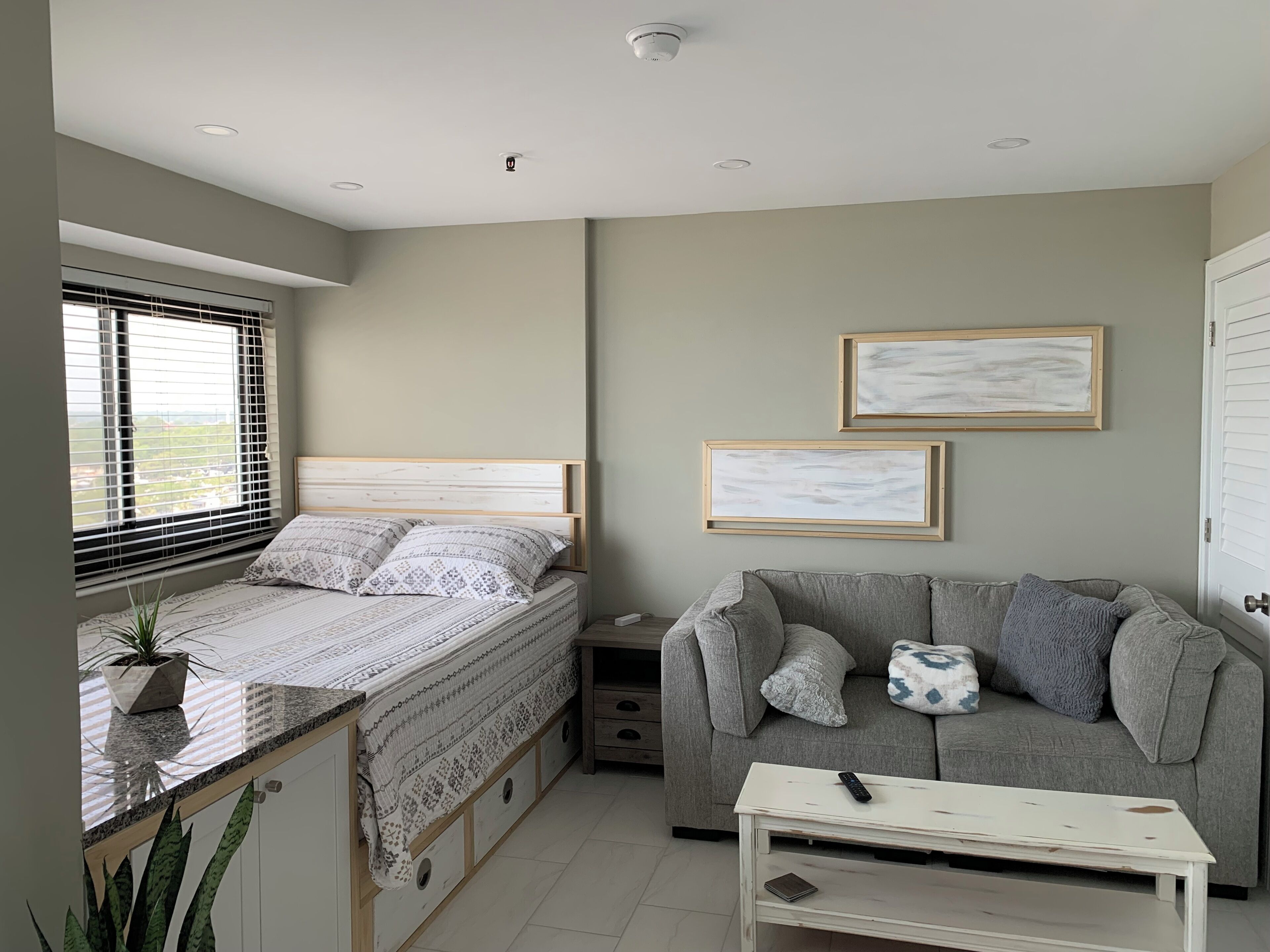 A bedroom with a bed, a grey sofa, a small table, and two framed pictures on the wall.
