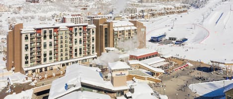 Un complejo turístico nevado con edificios de varios pisos, un telesilla y una zona de alquiler de motos de nieve.