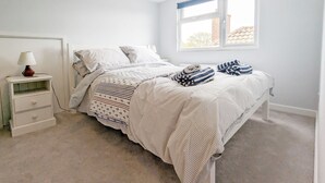 Een slaapkamer met een bed, nachtkastje, lamp en raam met uitzicht op gebouwen.