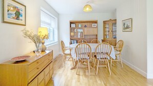 Een eetgedeelte met een houten tafel en stoelen, een kast met glazen deuren en een hanglamp.