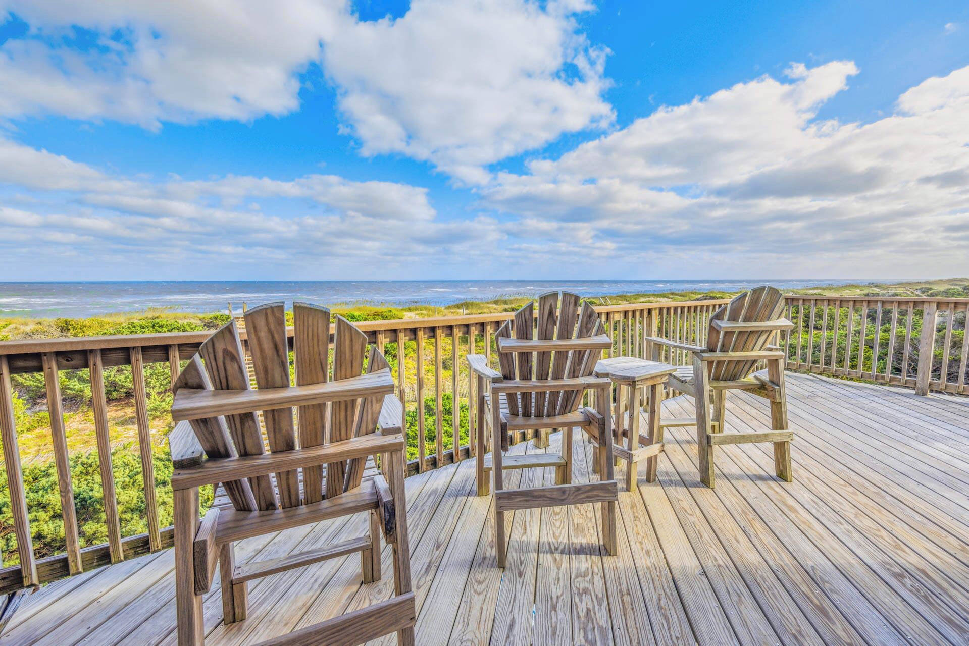 A wooden deck with Adirondack chairs overlooking a beach and ocean.