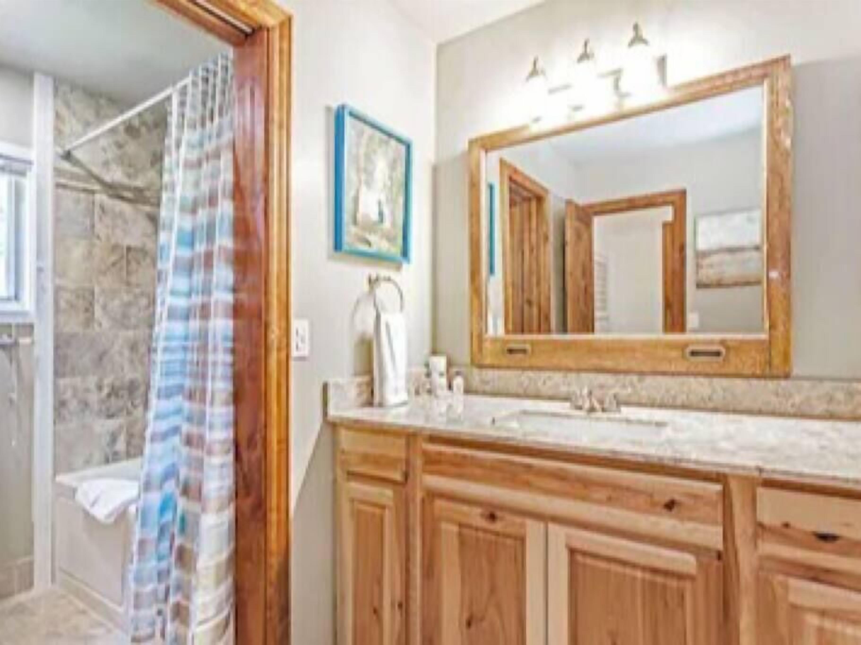 A bathroom with wooden cabinets, a large mirror, and a shower area.