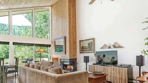Een knus woongedeelte met een grote bank, een open haard, een televisie en een eethoek met een tafel en stoelen.
