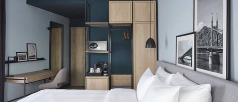 A modern hotel room with a bed, a desk, a wardrobe, and a framed picture of a bridge.