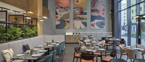 Un restaurante moderno con techos altos, amplios ventanales y una variedad de opciones de asientos, incluyendo cabinas y mesas.