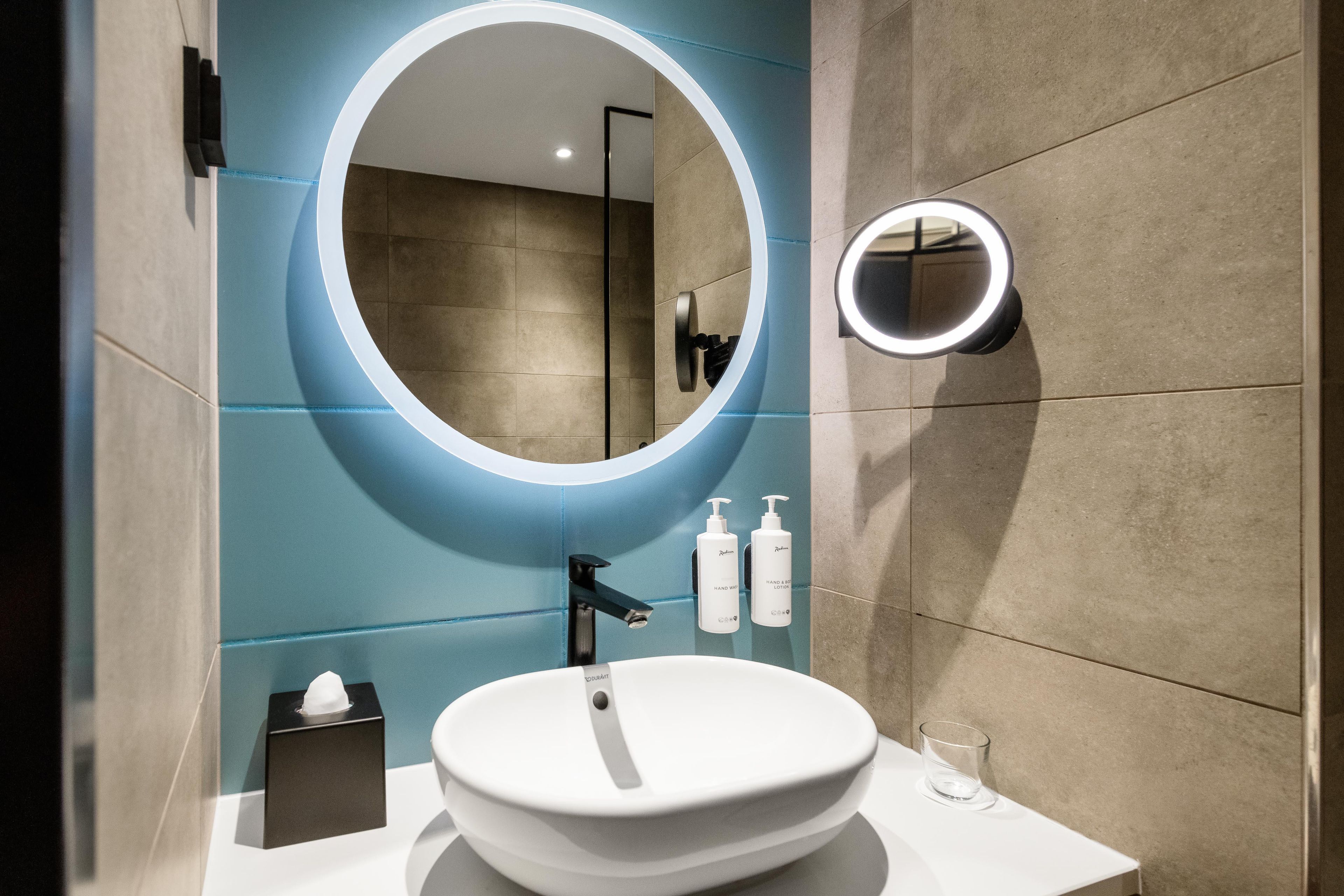 A modern bathroom with a round mirror, a sink, and two hand soap bottles.