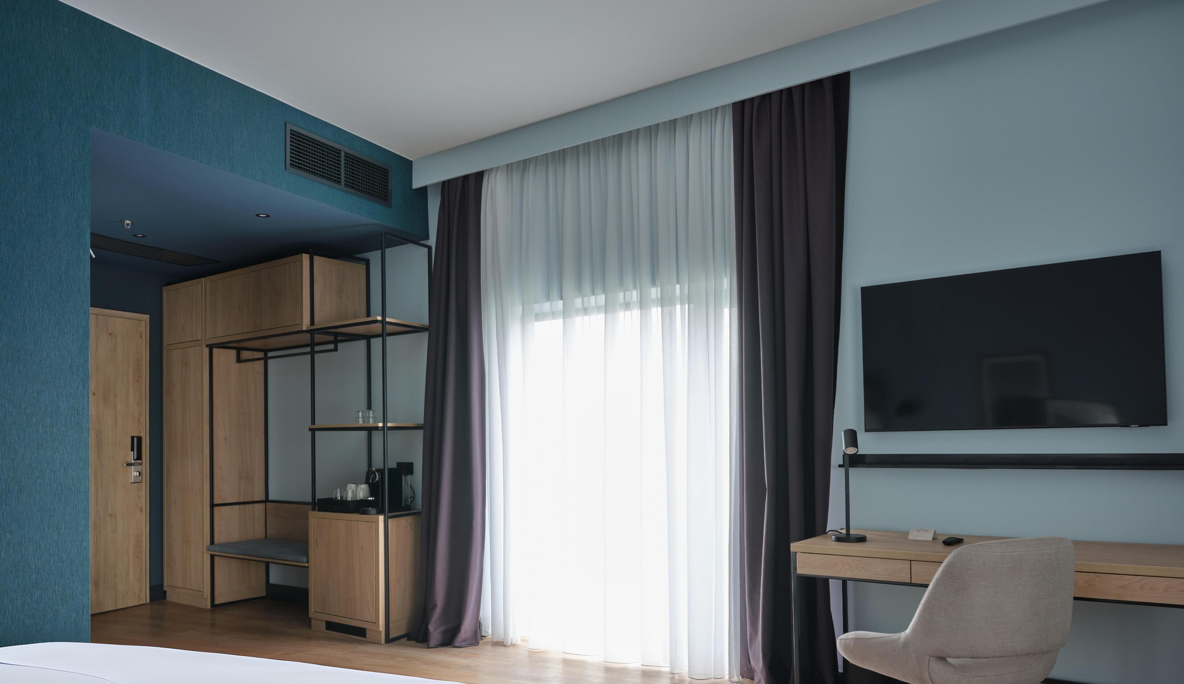 A modern room with a bed, a desk, a chair, a TV, and a wardrobe with shelves.