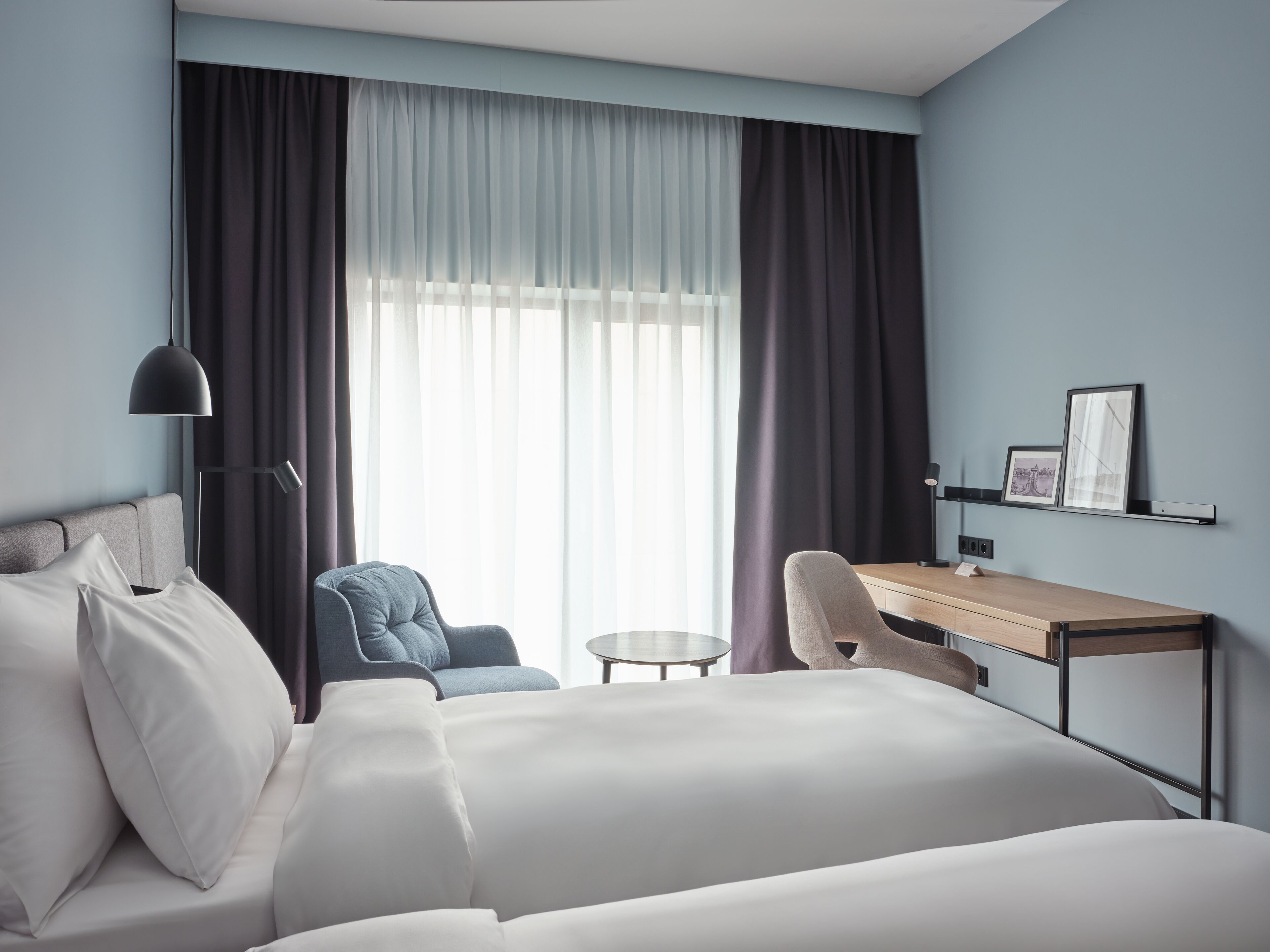 Una habitación de hotel con cama, dos sillones, un escritorio y un ventanal con cortinas.