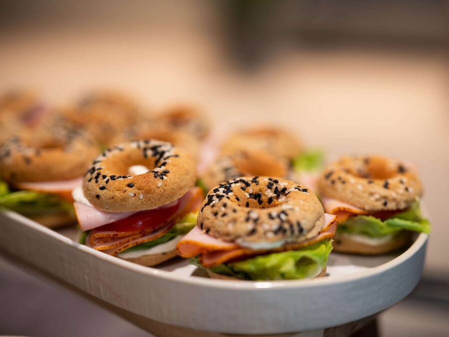 A tray of bagels with sesame seeds and cream cheese, accompanied by a sandwich with lettuce and tomato.