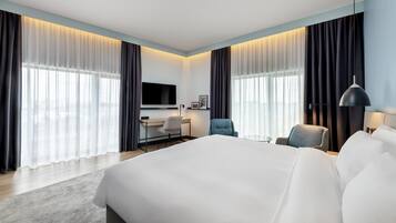 A modern hotel room with a large bed, a desk, a chair, and a TV.