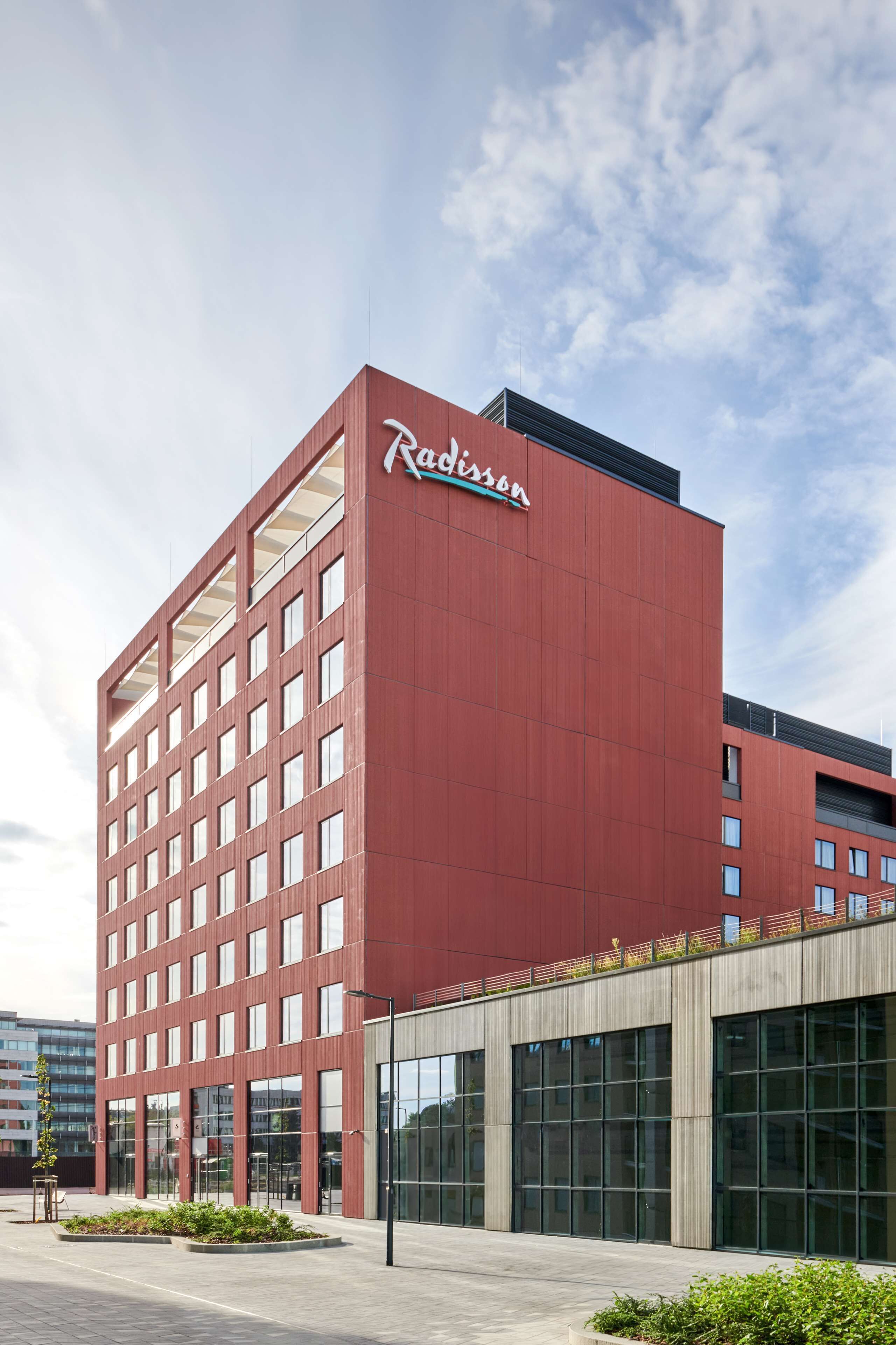 Un edificio de hotel rojo con diseño moderno, ventanas grandes y una señalización con el nombre visible.