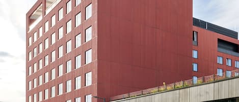 Un edificio de hotel rojo con diseño moderno, ventanas grandes y una señalización con el nombre visible.