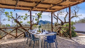 Ein Essbereich im Freien mit einem Tisch für vier Personen, umgeben von blauen Stühlen, unter einer Holzpergola mit Bergblick.