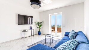 Ein modernes Wohnzimmer mit einem großen Fernseher, einem Sofa, einem kleinen Tisch und einer Zimmerpflanze.
