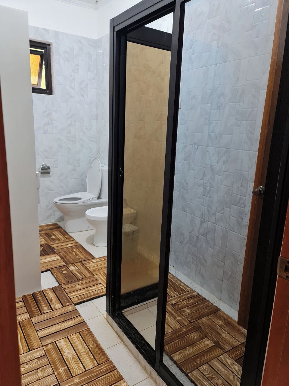 Un baño con inodoro, zona de ducha y suelo de madera.