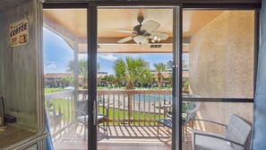 Un balcón con ventilador de techo, mobiliario exterior y vistas a una piscina y zonas verdes.
