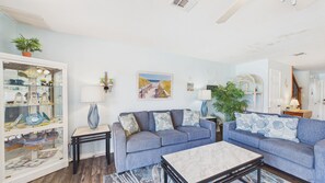 A living room with a blue sofa set, a glass display cabinet, and a painting of a beach pathway. - Paradise Pointe 137–5 Min to Beach–Sleeps 6 (Panama City Beach)