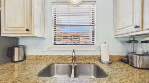 Una cocina con un lavamanos doble, una ventana con persianas, un hervidor, una licuadora y un tostador.