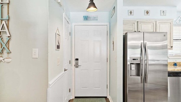 Un pasillo con una puerta blanca, un refrigerador de acero inoxidable y un letrero de bienvenida.