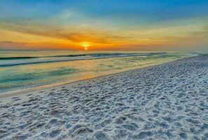 Una playa con atardecer, orilla arenosa y mar tranquilo.