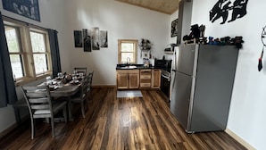 A spacious kitchen with wooden flooring, a stainless steel refrigerator, and a dining area with a table and chairs.