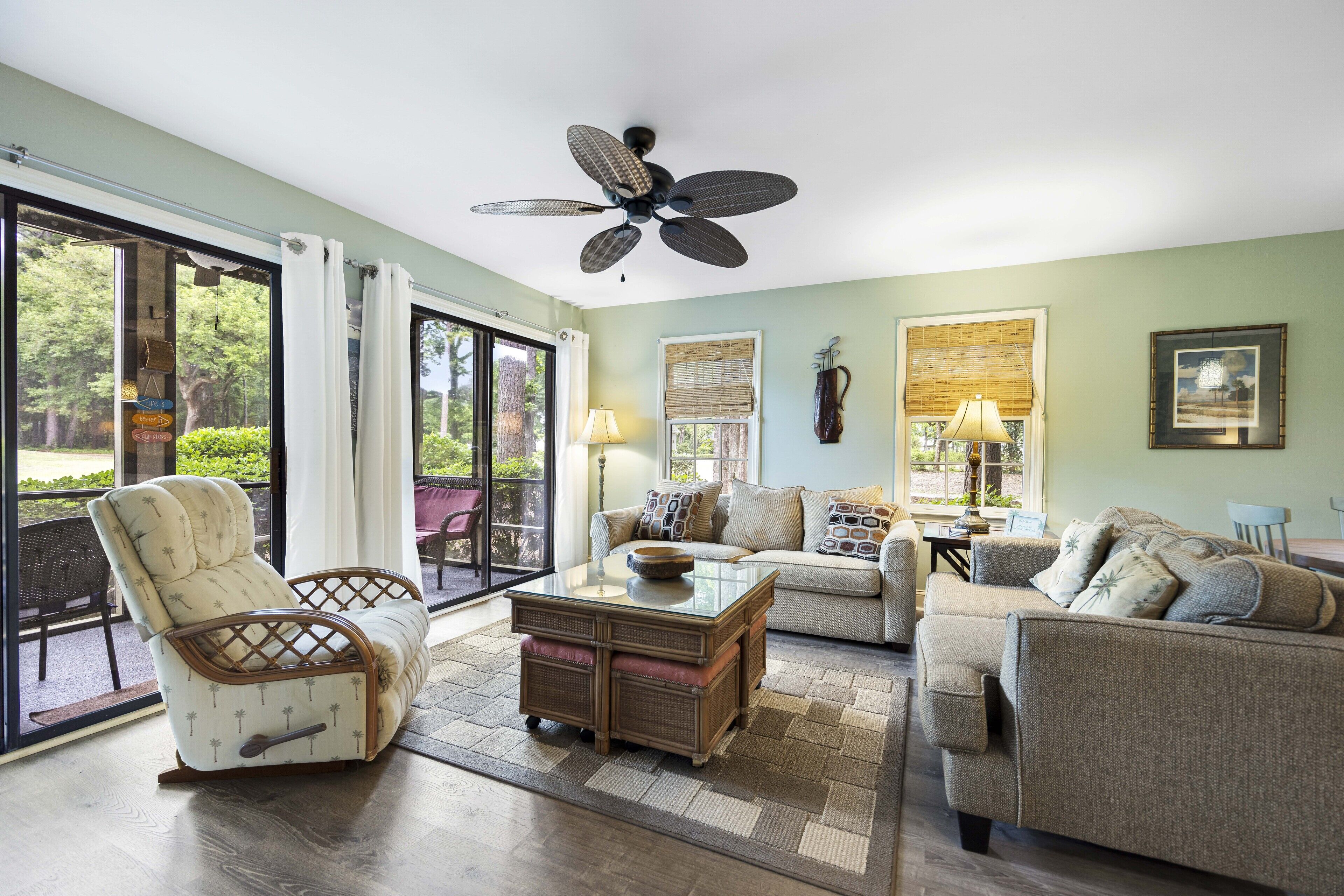 A spacious living room with a glass door leading to a patio, a ceiling fan, and a large window with blinds.