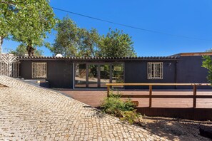 A building with a tiled roof, a wooden deck, and a paved area with a bench.