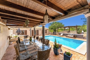 Un espace extérieur avec une piscine, une table en verre et des chaises en osier, entouré de plantes en pot et agrémenté d’une pergola.